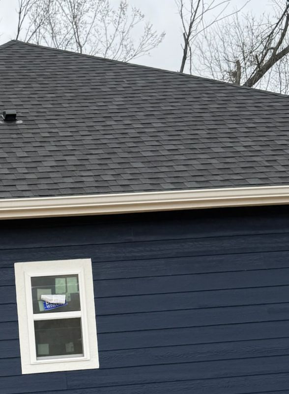 Finished dark shingle roof with a white gutter above navy blue siding and a white window