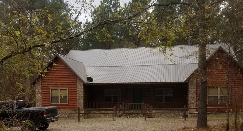 Single story log cabin with a silver metal roof and a covered front porch among the trees