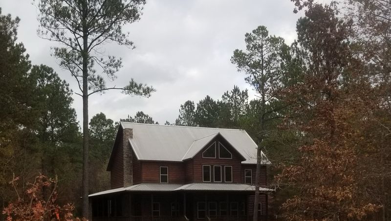 Two story log home with a silver metal roof, surrounded by tall pine trees
