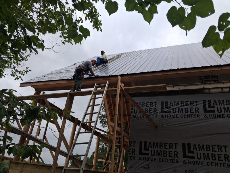 Two Pacheco Roofing workers installing metal roof panels on a new building